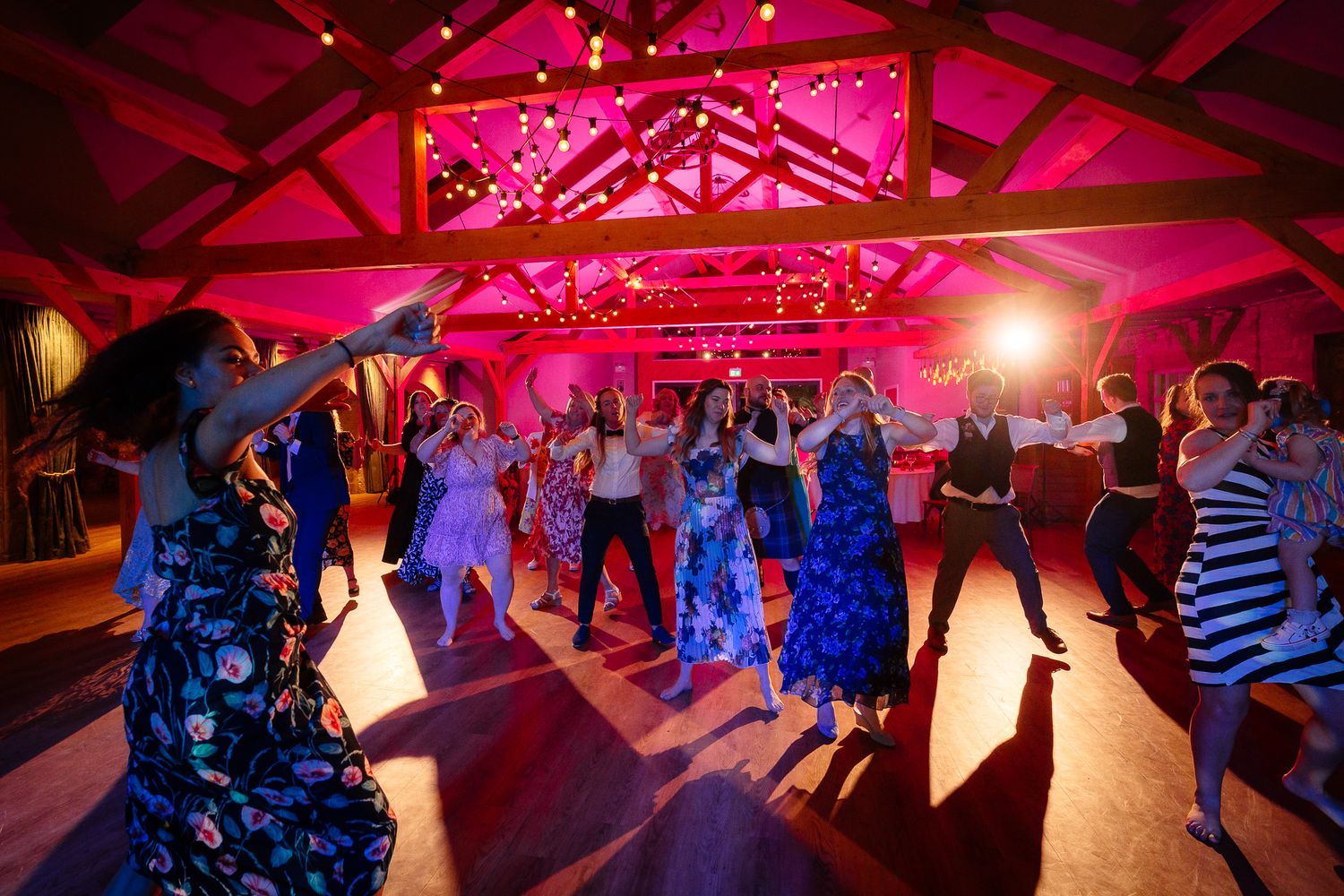 Dance floor illuminated with vibrant pink and blue lighting during evening wedding celebration.