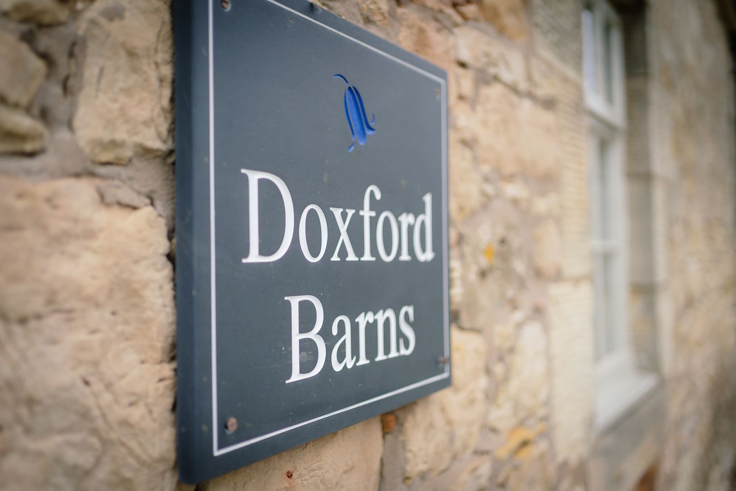 Rustic stone wall with directional signs for 'Doxford' and 'Barns' mounted on it. Doxford Barns
