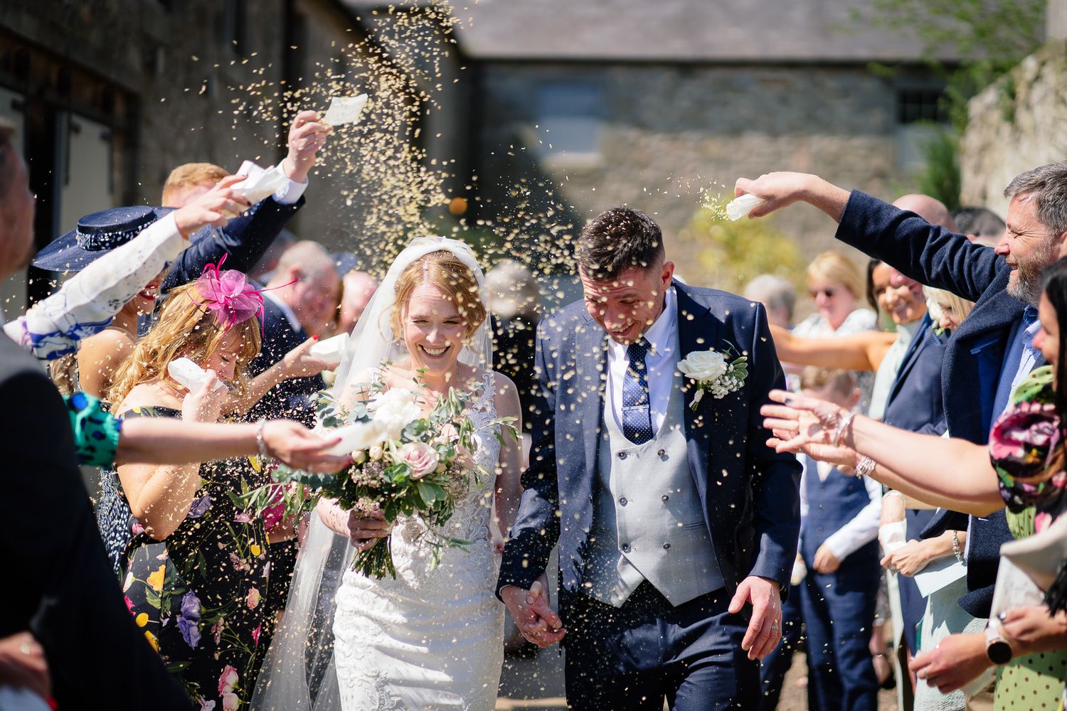 Wedding guests throw confetti during outdoor celebration.