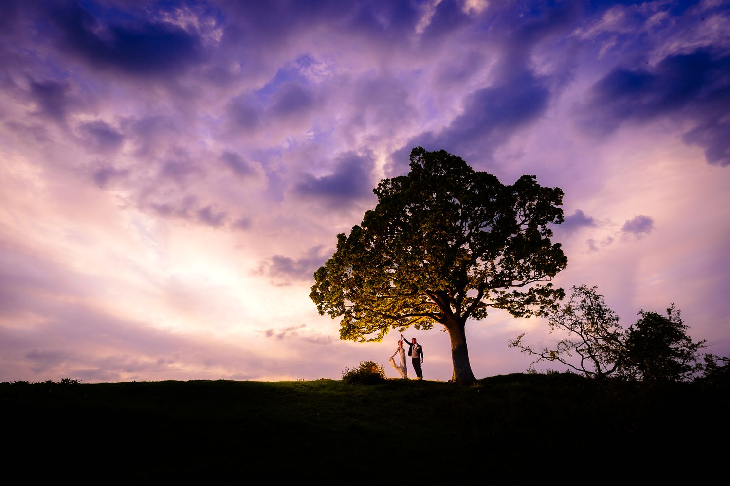 Dramatic purple sunset sky creates silhouette backdrop for wedding photography.