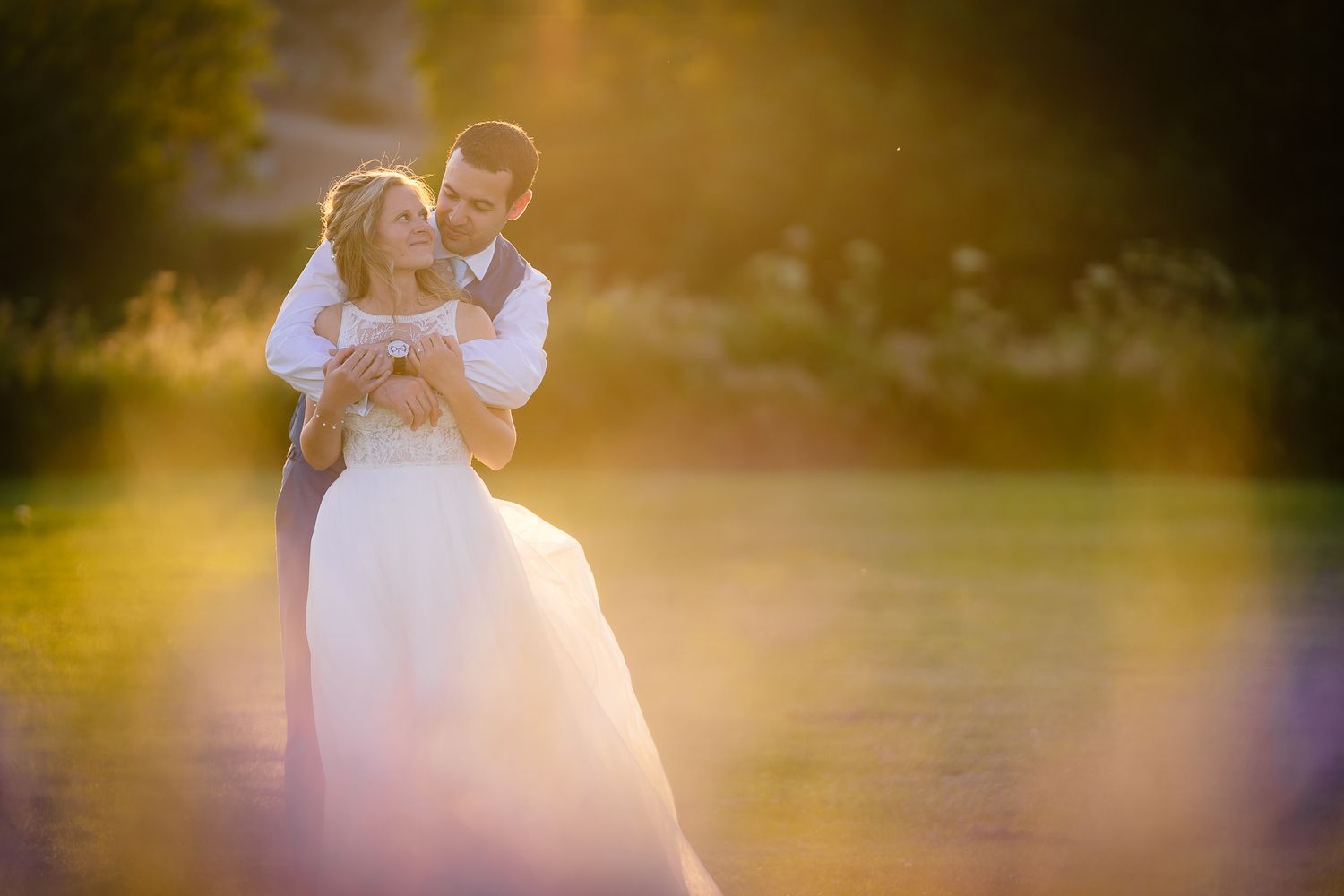 Romantic wedding couple embraces in golden sunlight during outdoor photo session. Doxford Barns