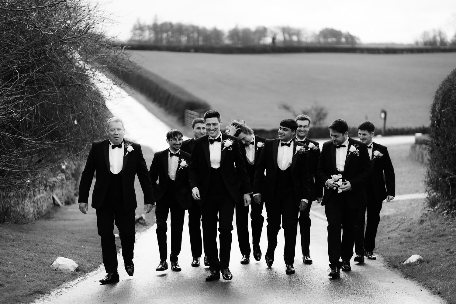 Wedding party in formal attire walks together along countryside path. Doxford Barns