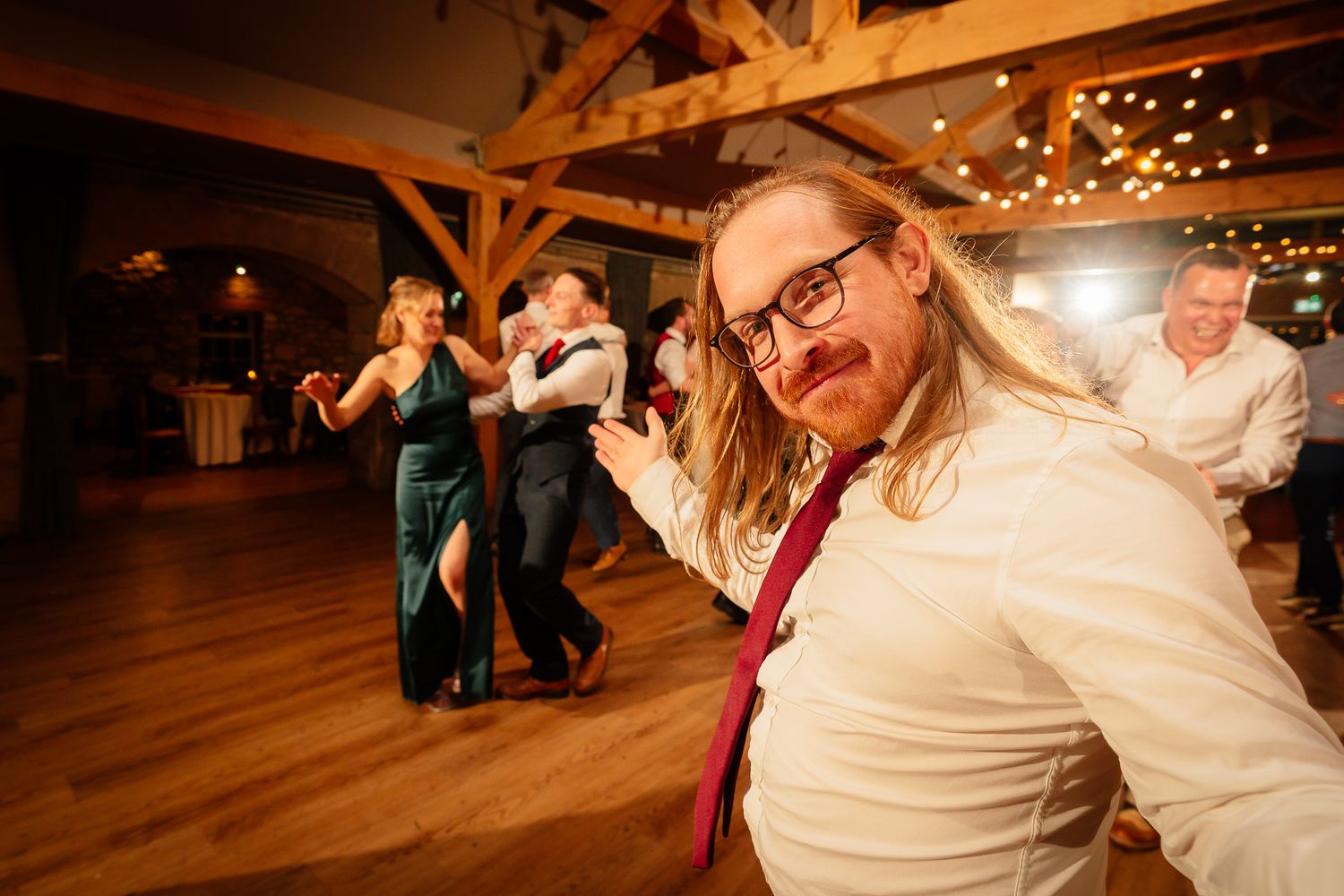 Wedding guests dancing and celebrating on a wooden dance floor under string lights. Doxford Barns