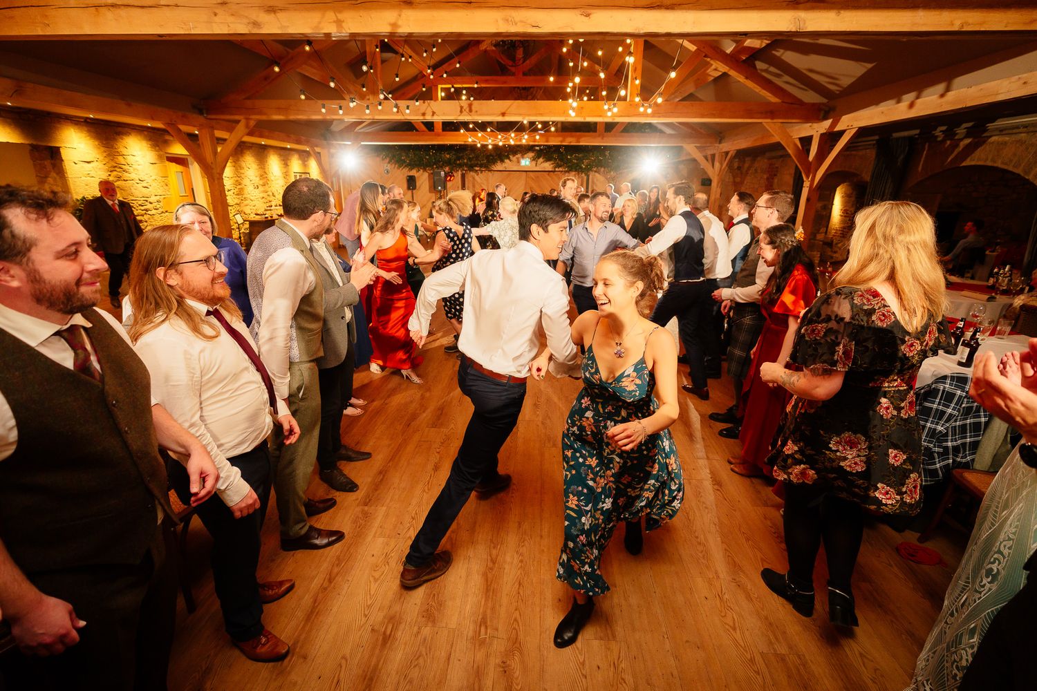 Wide shot of wedding reception dance floor with guests celebrating under string lights. Doxford Barns