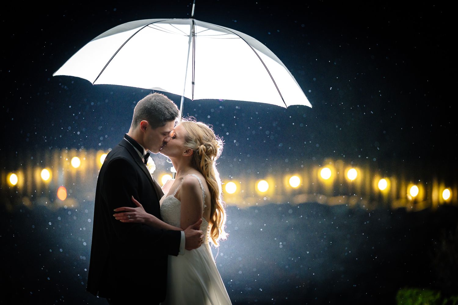 Romantic couple dancing under white umbrella with twinkling lights in background. Doxford Barns