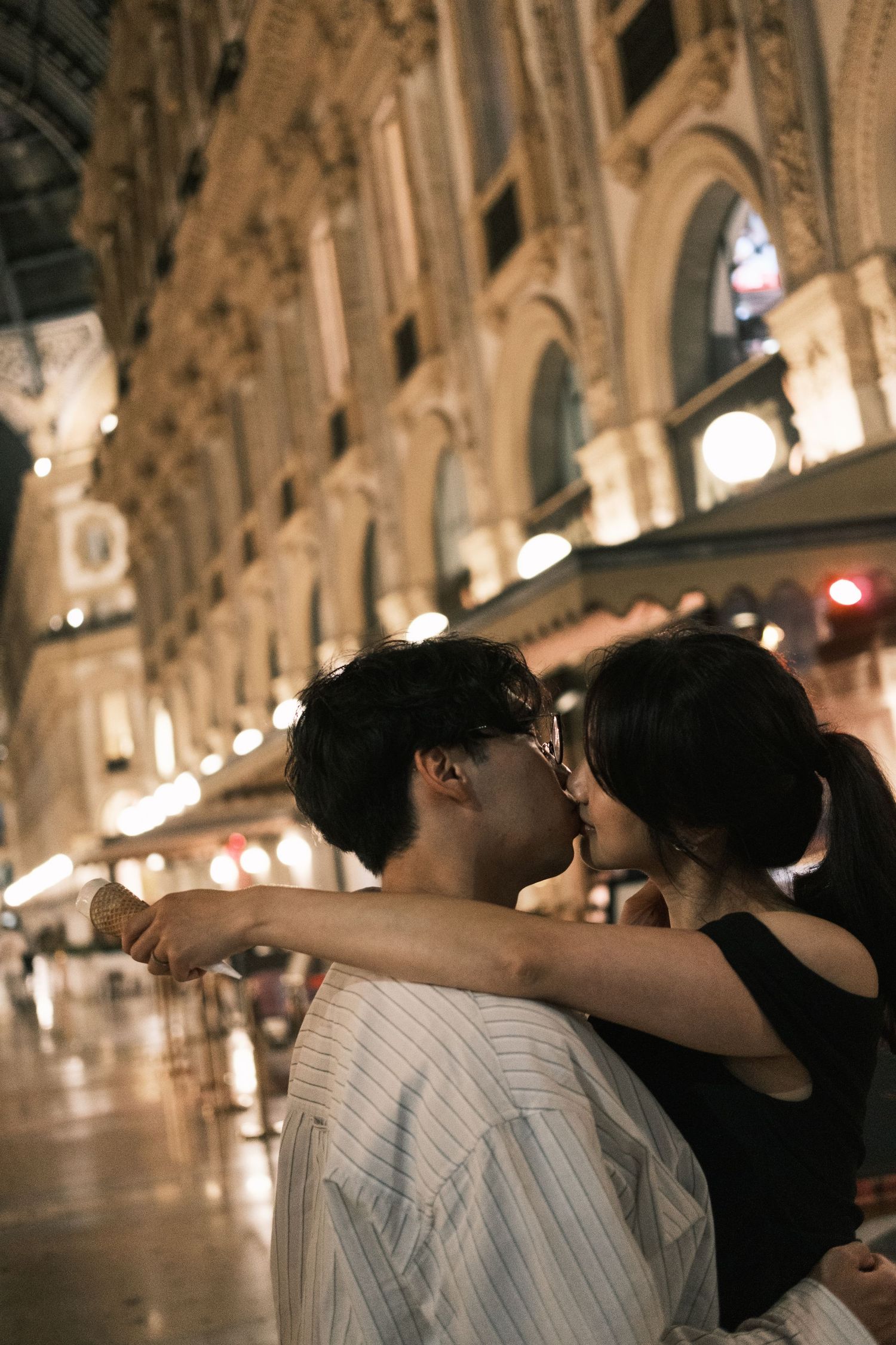 A romantic evening embrace under the ornate arches and glowing lights of a historic European arcade.