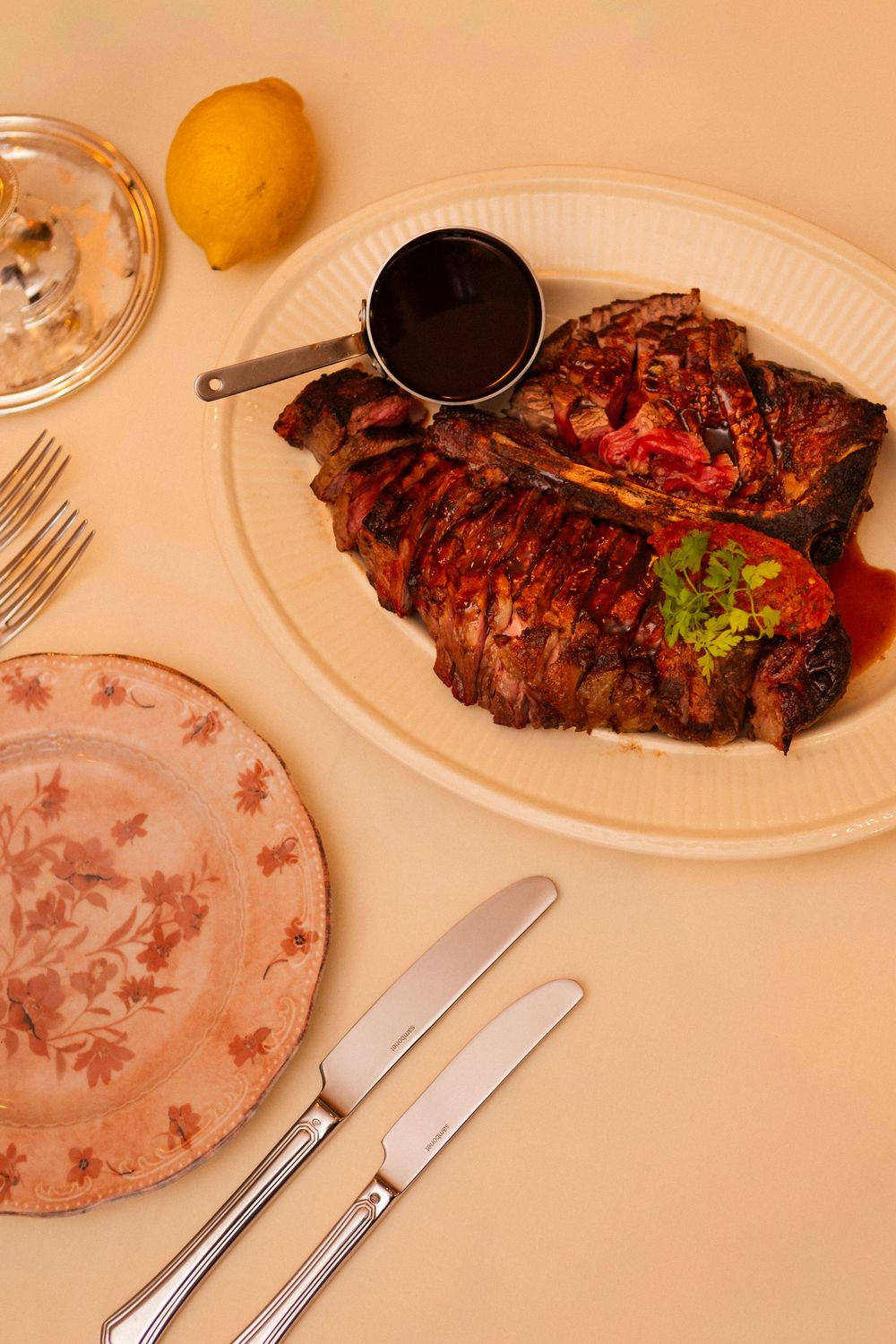 A juicy grilled steak served on a white plate with floral pattern details and cutlery.