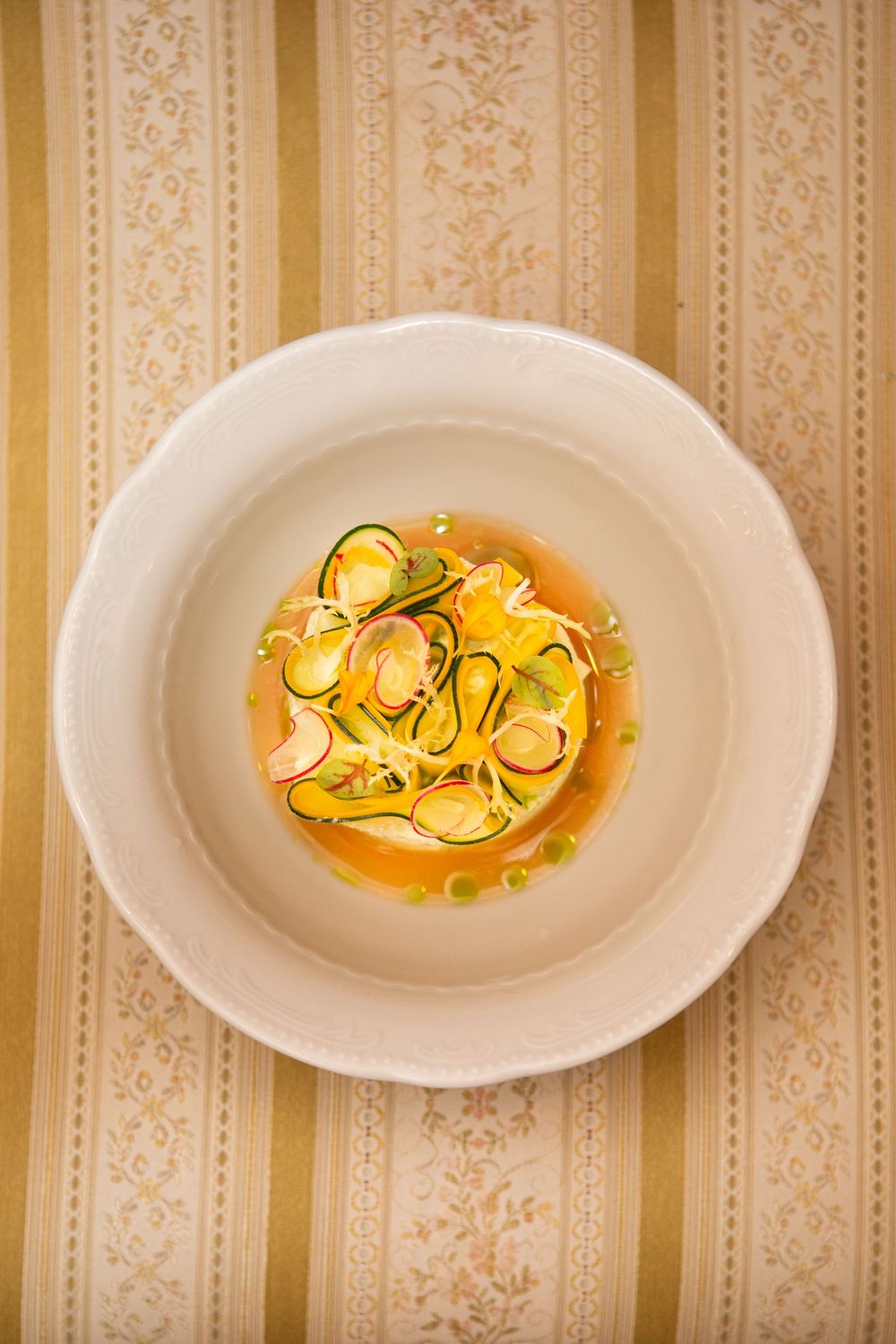 Three white plates with delicate tortellini pasta in a yellow sauce garnished with fresh herbs on a striped wallpaper background.