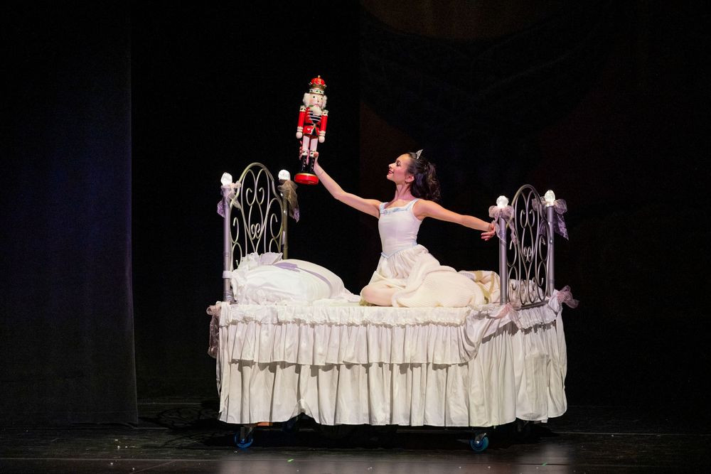 Ballet dancers perform dramatic scenes on stage with elegant white bedding and theatrical lighting.