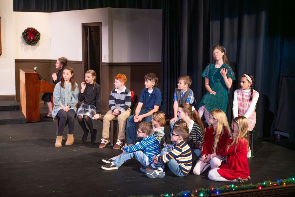 A group sits together on a stage with festive holiday lights decorating the edge of the performance space.