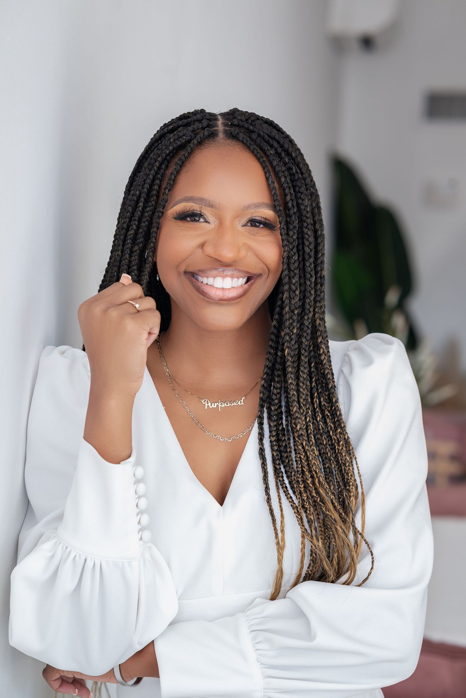 Professional portrait series in white showing a bright smile and braided hairstyle against a light background.