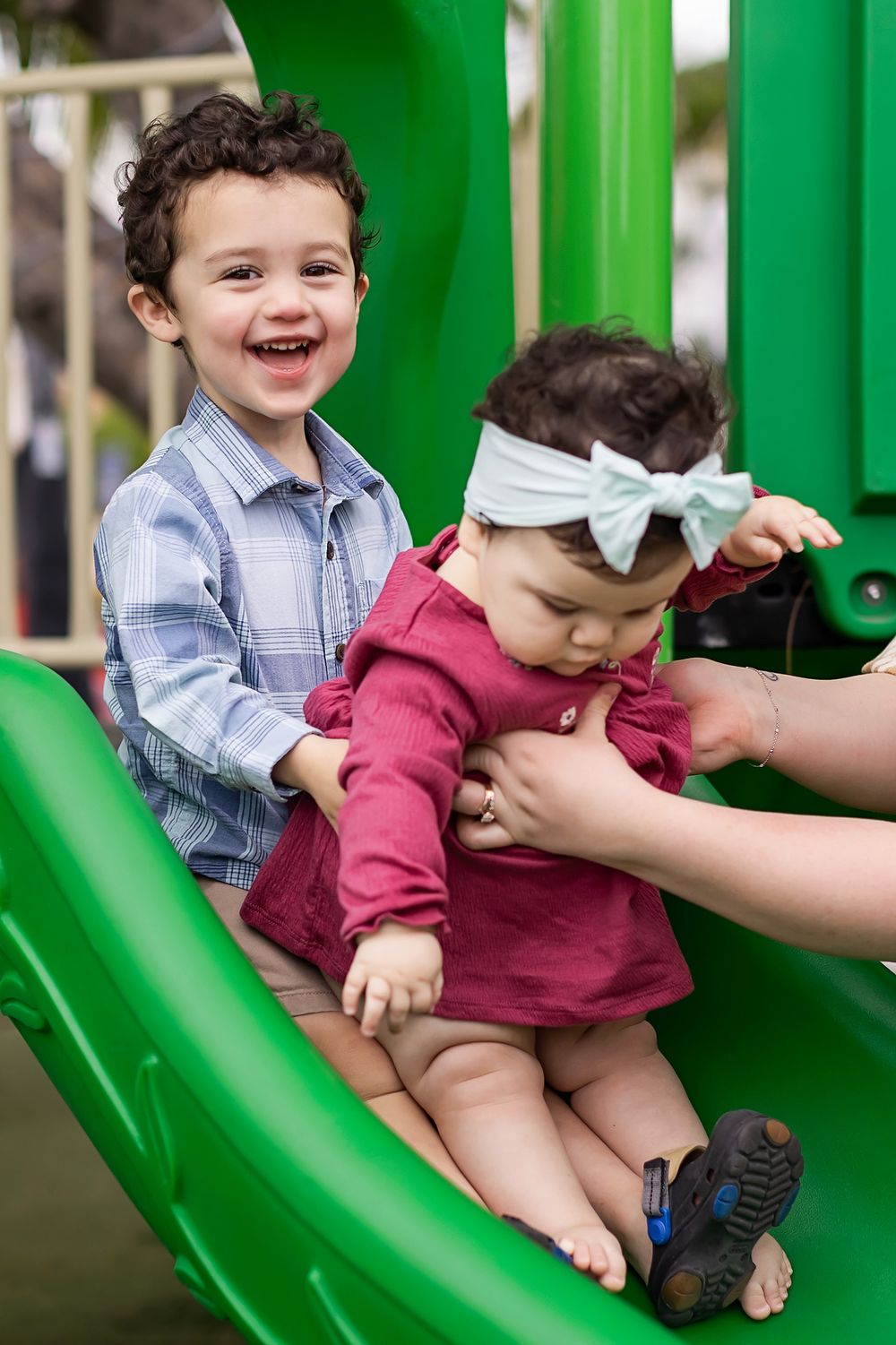 Two children share a joyful moment while playing together on a bright green playground slide.