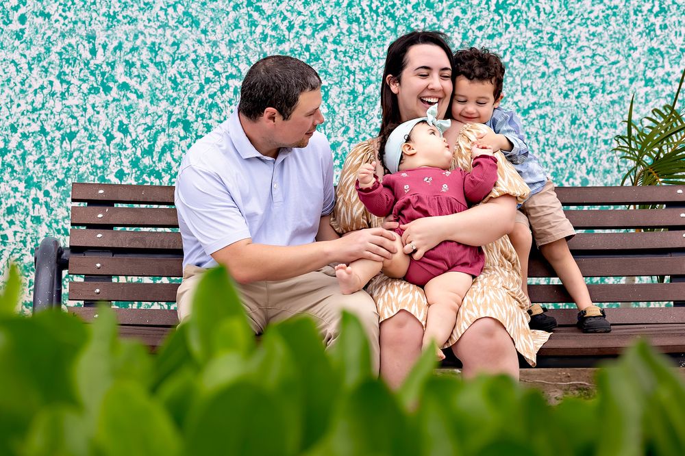 Family enjoying a relaxed moment together while sitting on a wooden park bench surrounded by greenery.