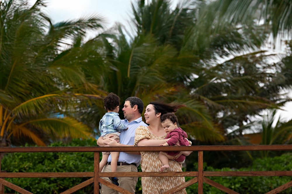 A couple shares a romantic moment on a railing with tropical palm trees in the background at sunset.
