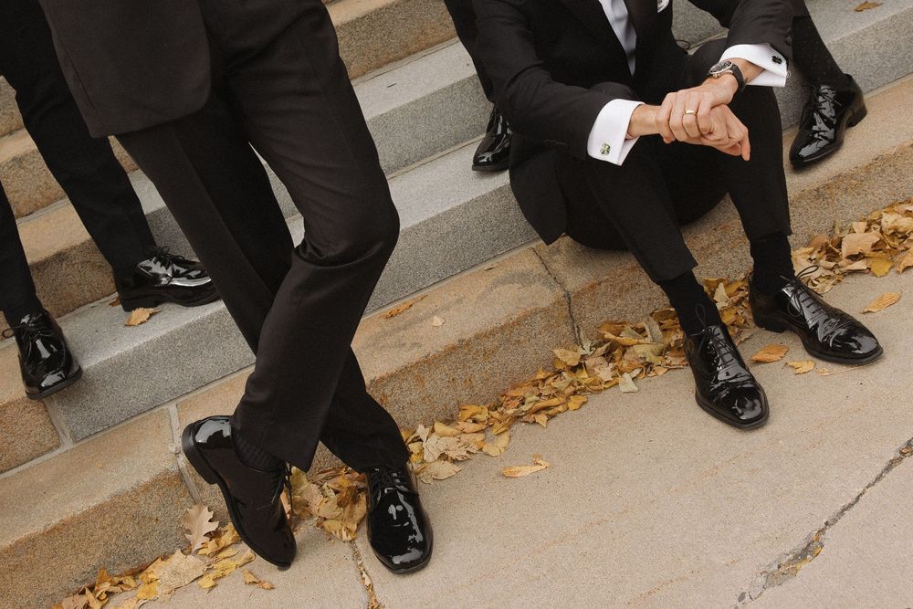 Close-up view of formal black dress shoes and suit pants on stone steps with scattered autumn leaves.