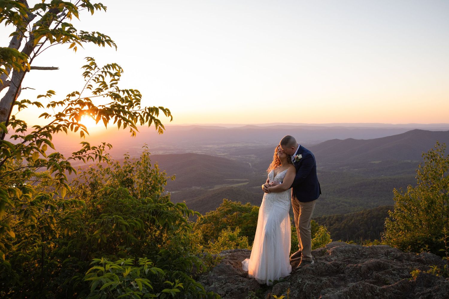 Sunset mountain landscape with silhouetted trees and rolling hills in the distance.