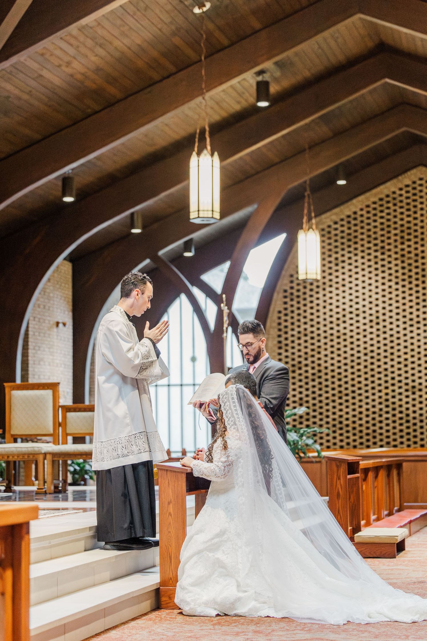 Couple praying together in a church with vaulted wooden ceilings and pendant lighting.