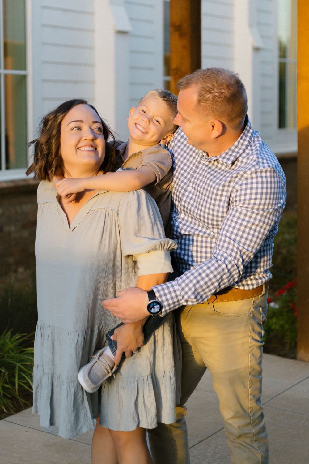 Family shares joyful moment together outside white church building in warm sunlight.