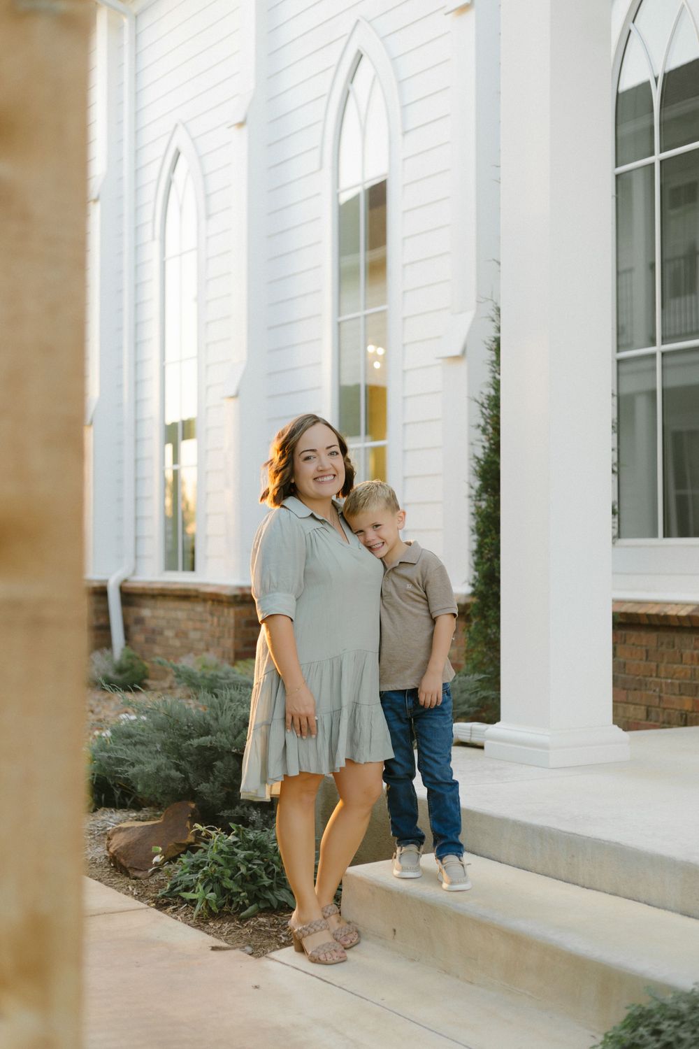Parent and child stand together on church steps next to white pillars.