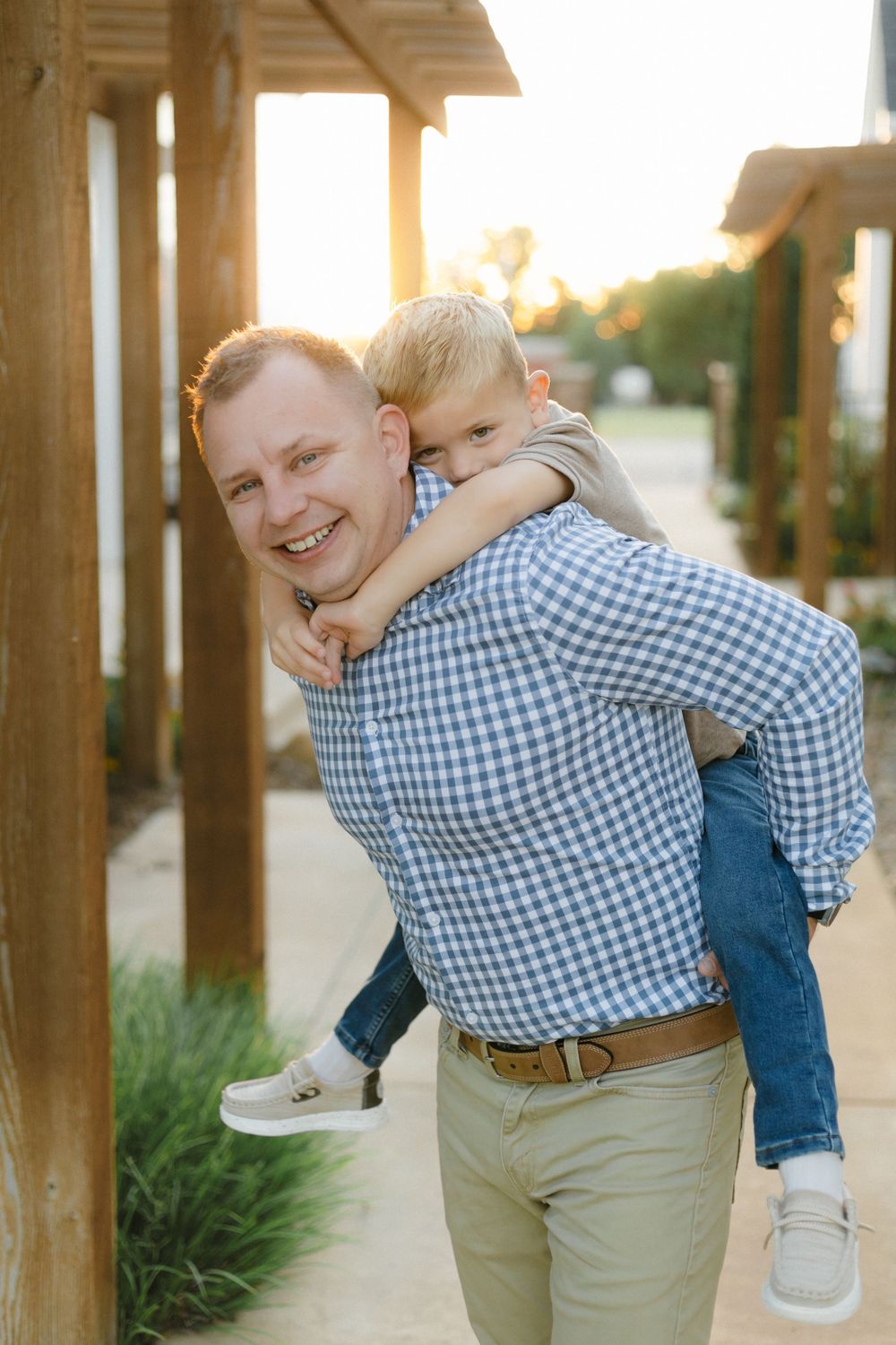 Parent gives child piggyback ride along outdoor walkway during golden hour.