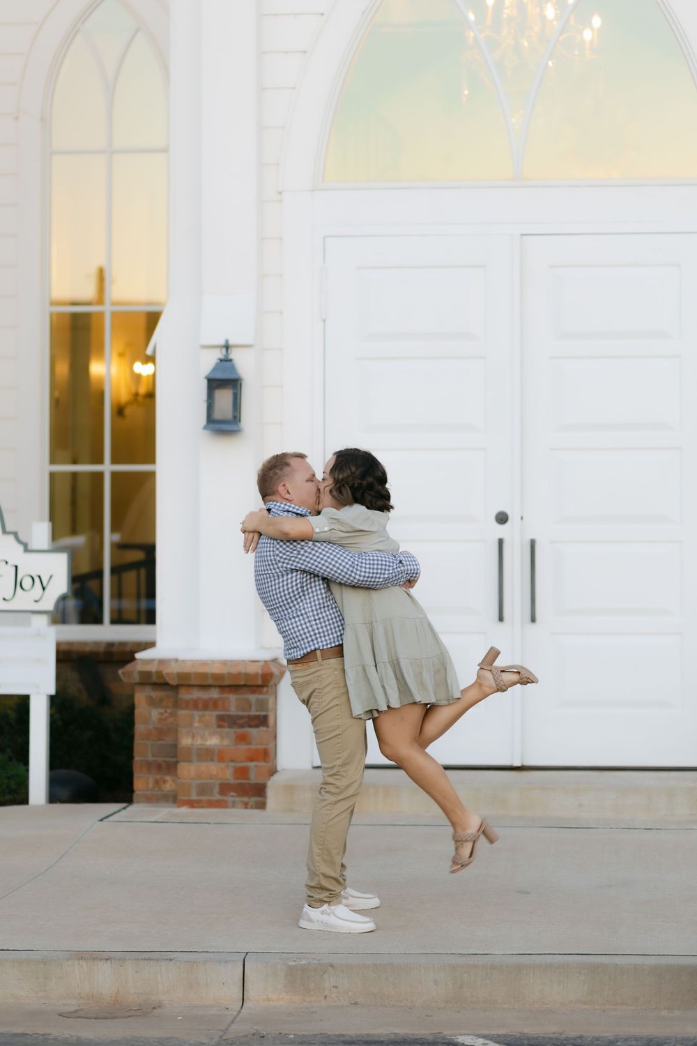 Couple embraces in romantic moment outside white church doors at sunset.