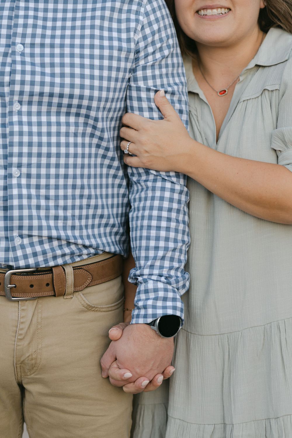 Close-up of couple holding hands showing blue gingham shirt and gray dress details.