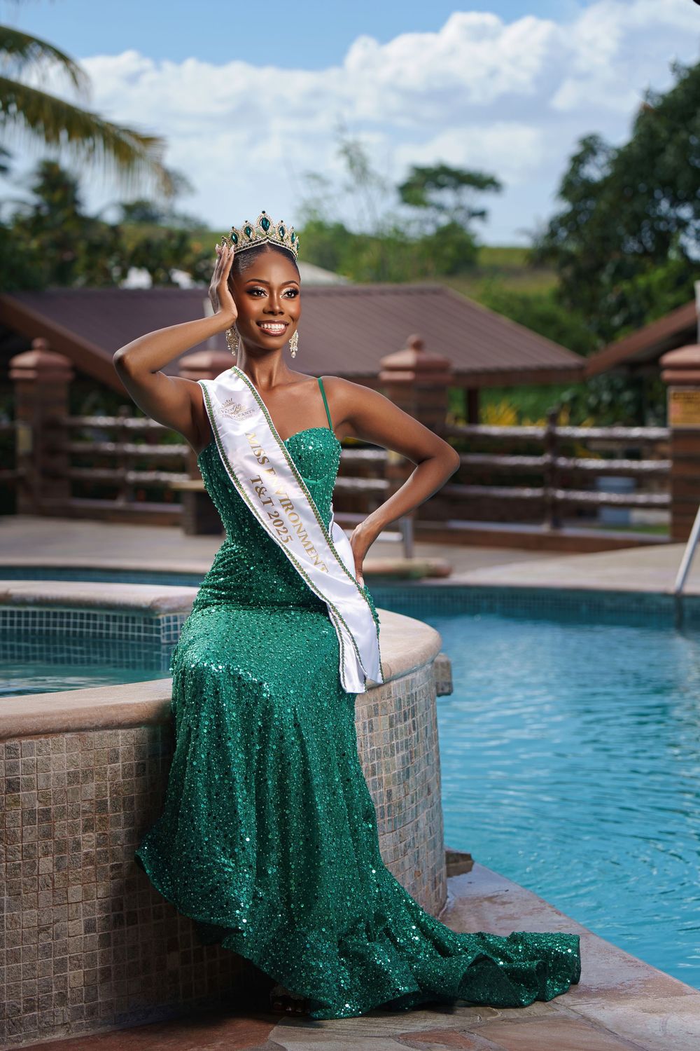 Beauty pageant contestant in a sparkling emerald green gown poses elegantly by a swimming pool.