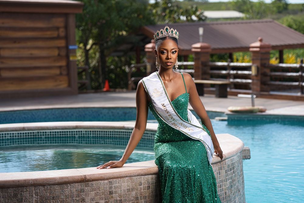 A person in a sparkly green evening gown poses elegantly by a swimming pool on a sunny day.