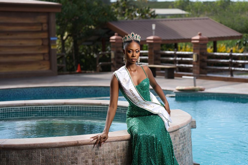 Pageant contestant in a sequined green gown and sash sits gracefully by a resort pool.