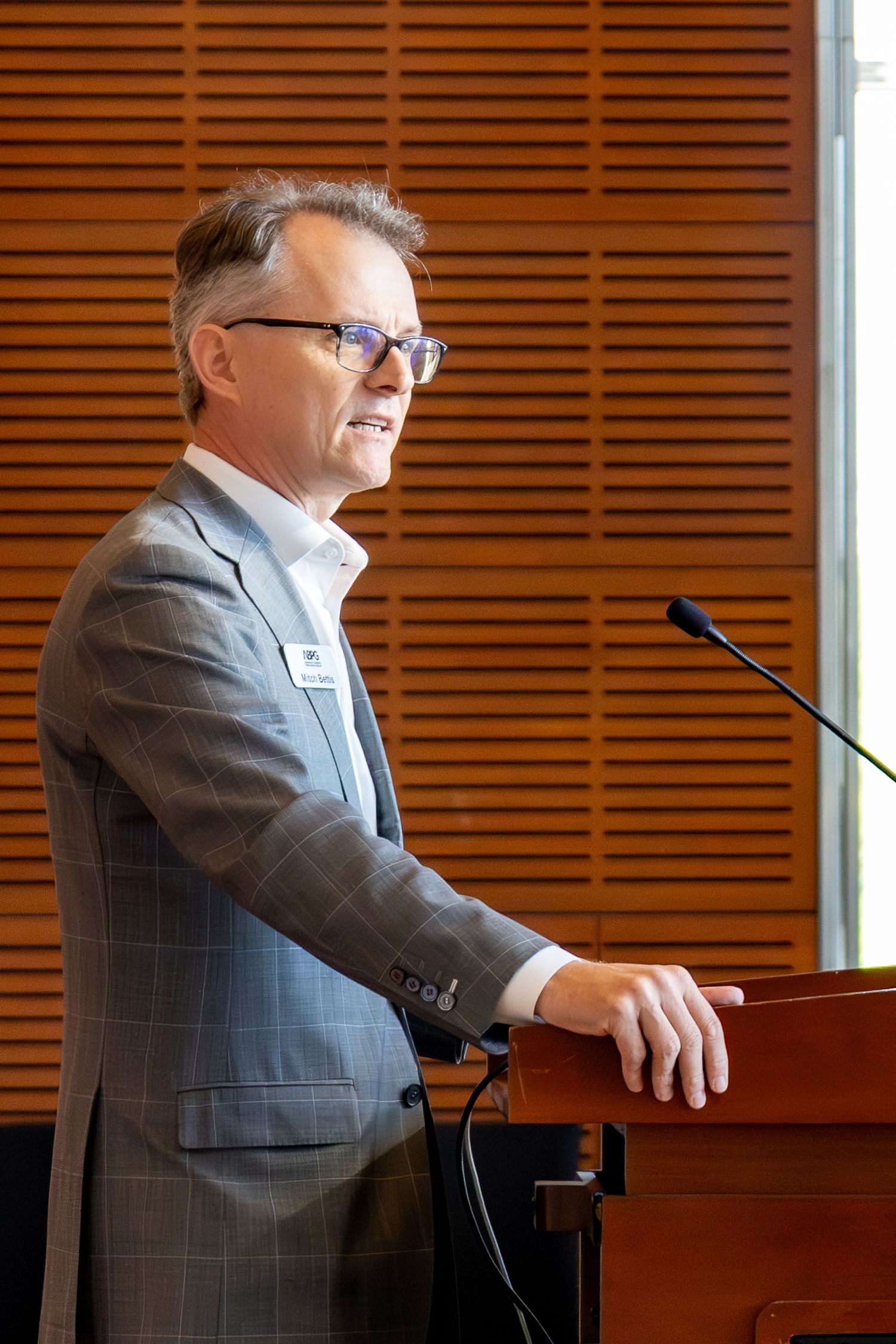 Speaker at a podium gives an engaging presentation in front of wood paneled walls in a professional setting.
