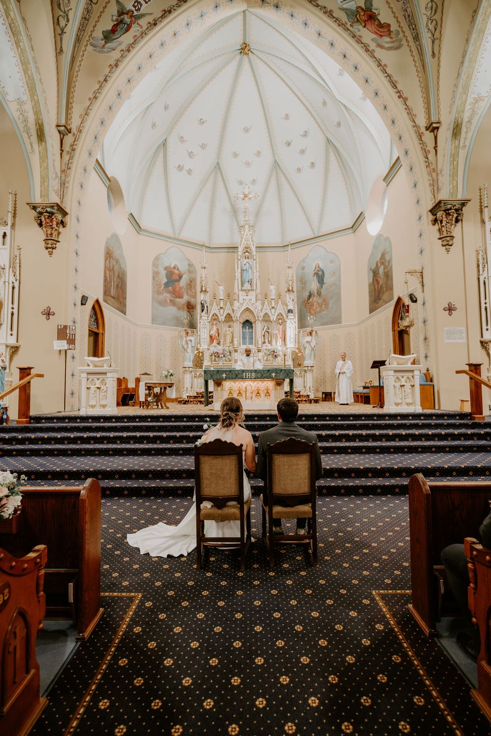 bride and groom front and center sit on chairs in front of the altar