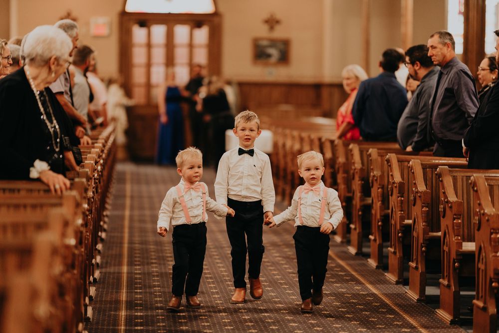 3 little blond ring bearers walk down the aisle.