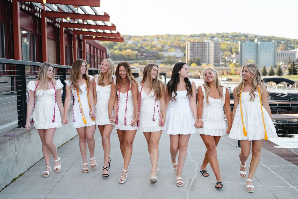 A group of people wearing white dresses and pink accessories walking together on a sidewalk.