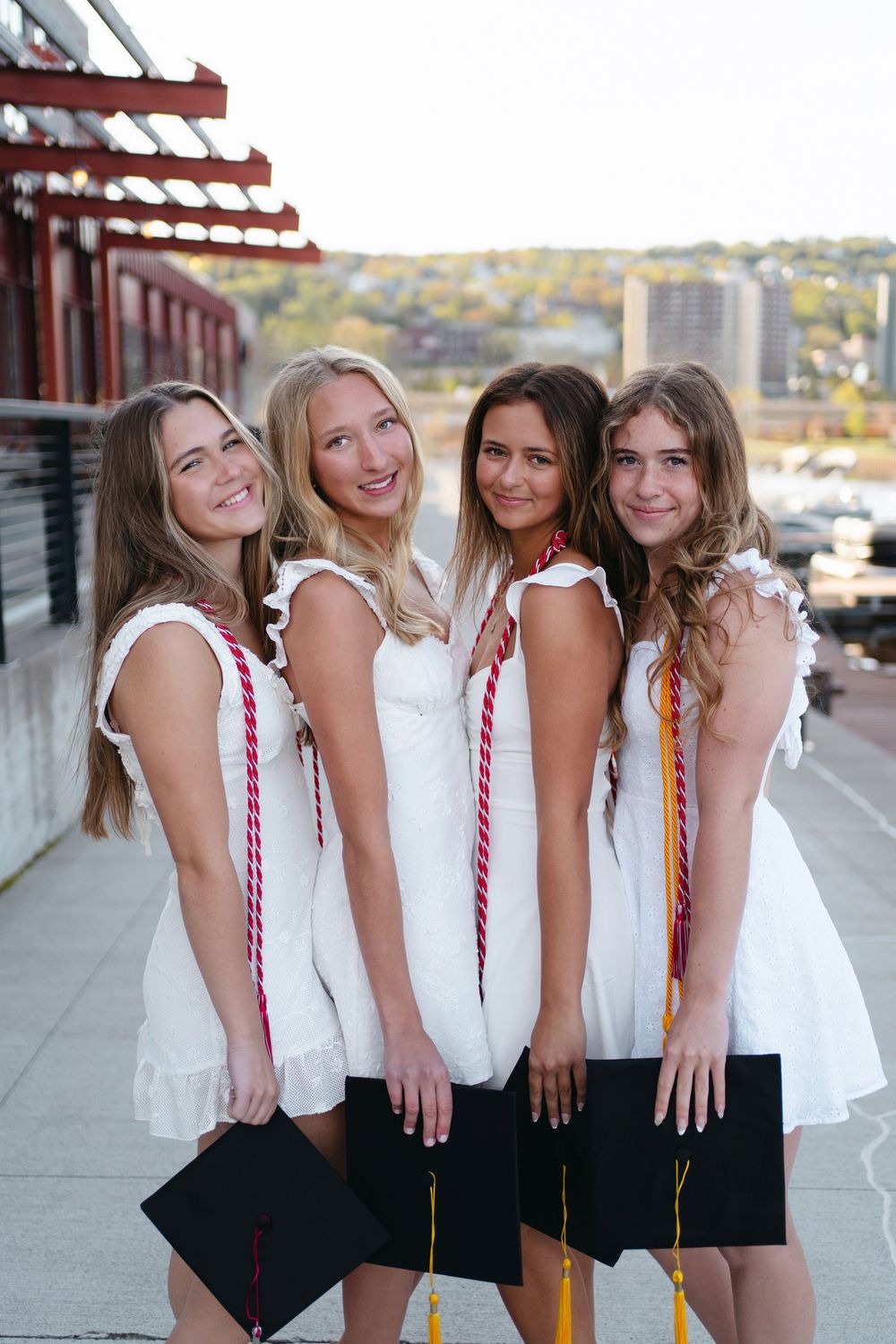 Four friends in white tops and black bottoms pose with colorful braided ribbons in their hair.