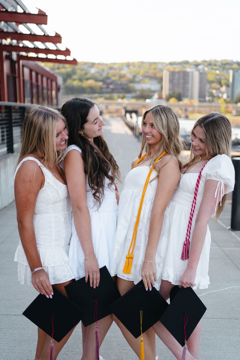 A group in matching white tops and black bottoms laughs together while posing outdoors near a waterfront.