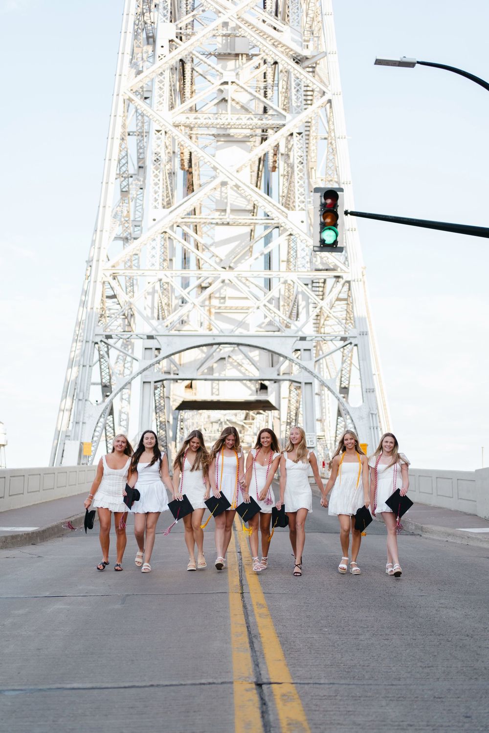 A group in white dresses walking together on a bridge with metal architecture in the background.