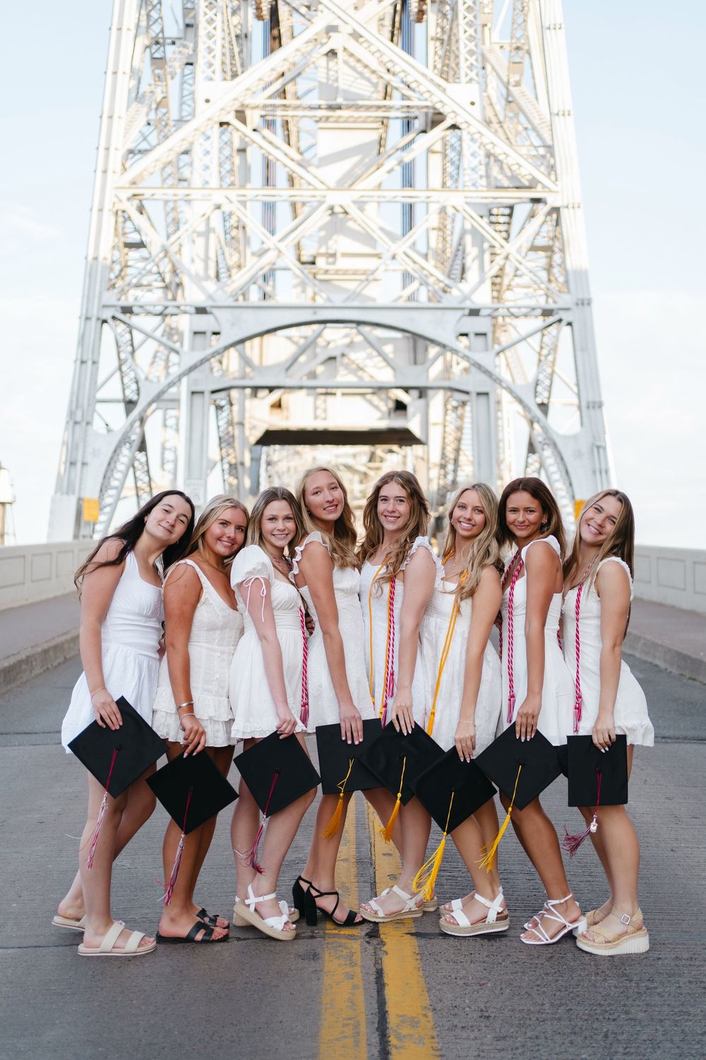 A group in white tops and black bottoms poses playfully together on a bridge with yellow road markings.