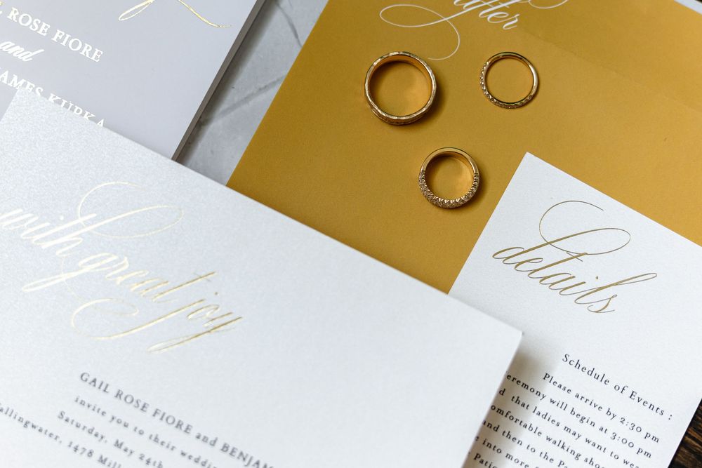 Wedding invitation suite featuring elegant white and gold stationery with calligraphy and wedding rings on display.