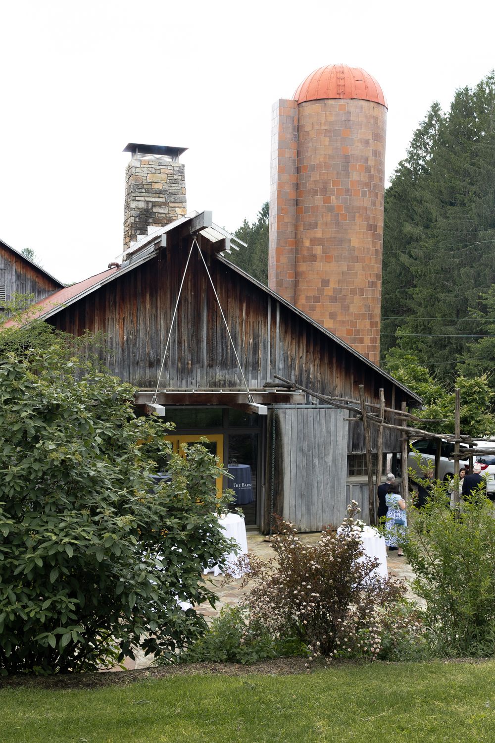 Four views of a rustic wooden barn with brick silos and lush greenery surrounding the weathered structure.