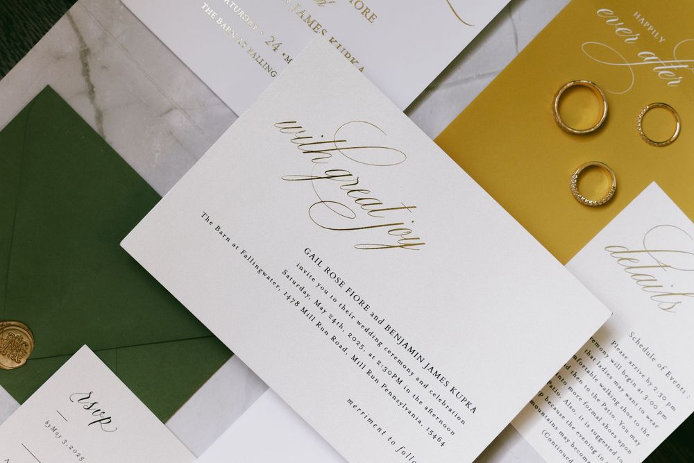 Elegant wedding invitation suite featuring gold and emerald green colors with calligraphy details and wedding rings.