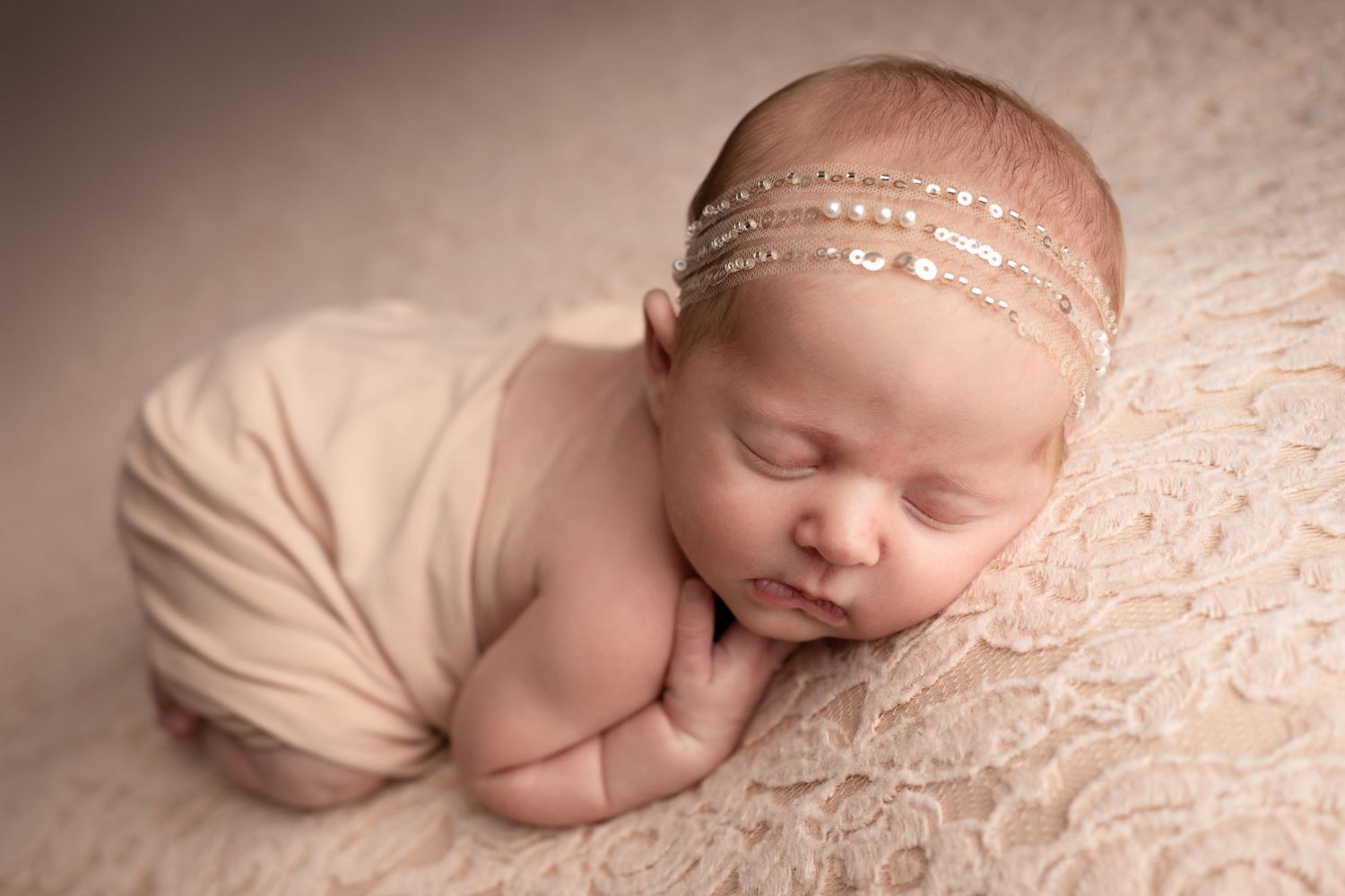 A sleeping baby in pink ruffled outfit lies on white fur between two plush elephant toys.