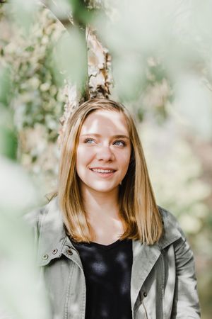 A person wearing a gray jacket poses against a dreamy spring background with soft bokeh and blossoming flowers.