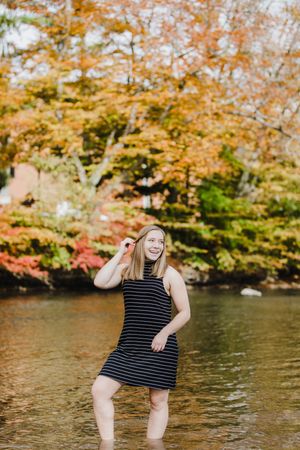 Playful outdoor photoshoot by a lake with autumn foliage featuring someone in a striped dress.