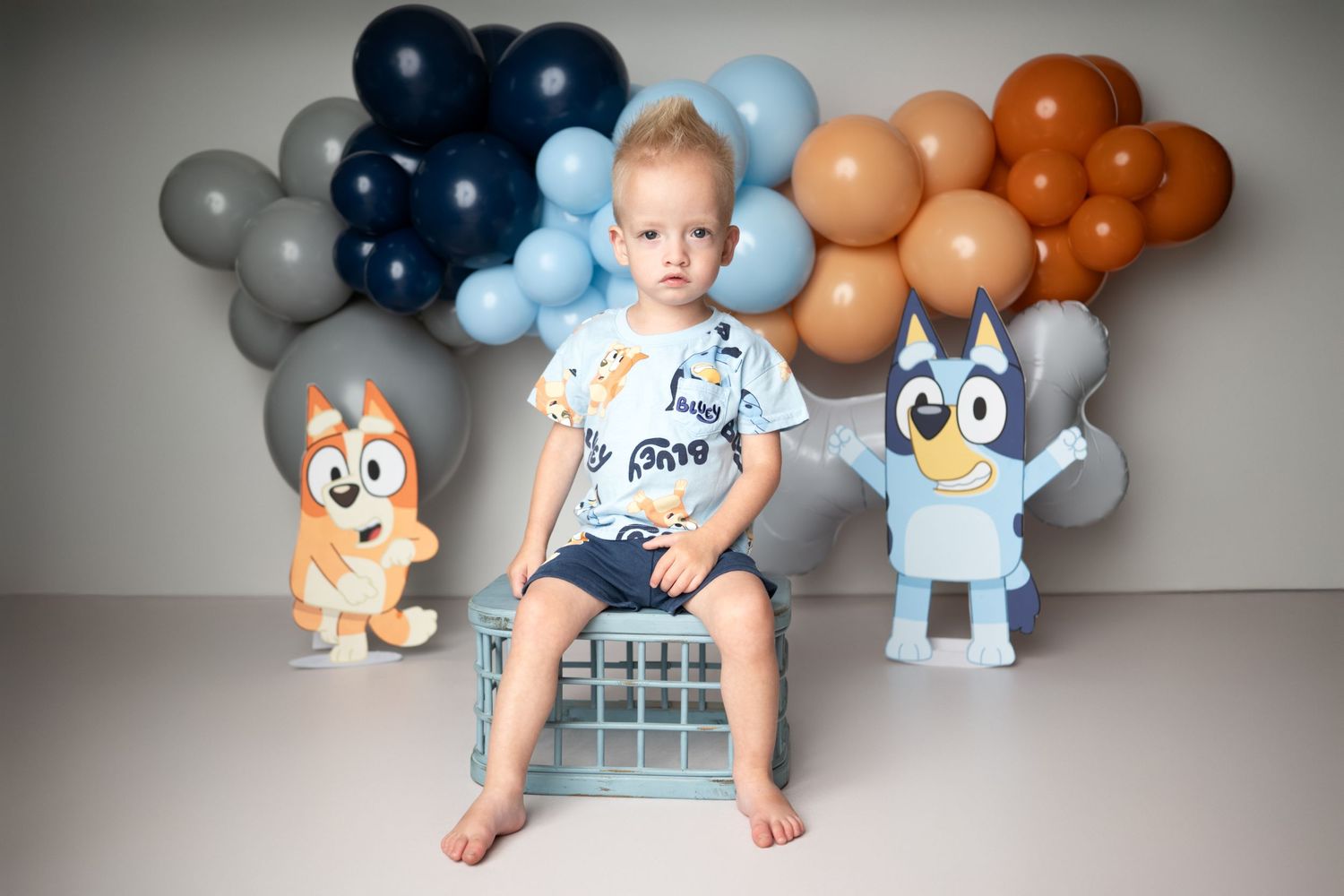 A baby's first birthday party setup with navy and orange balloons and woodland animal decorations against a gray wall.