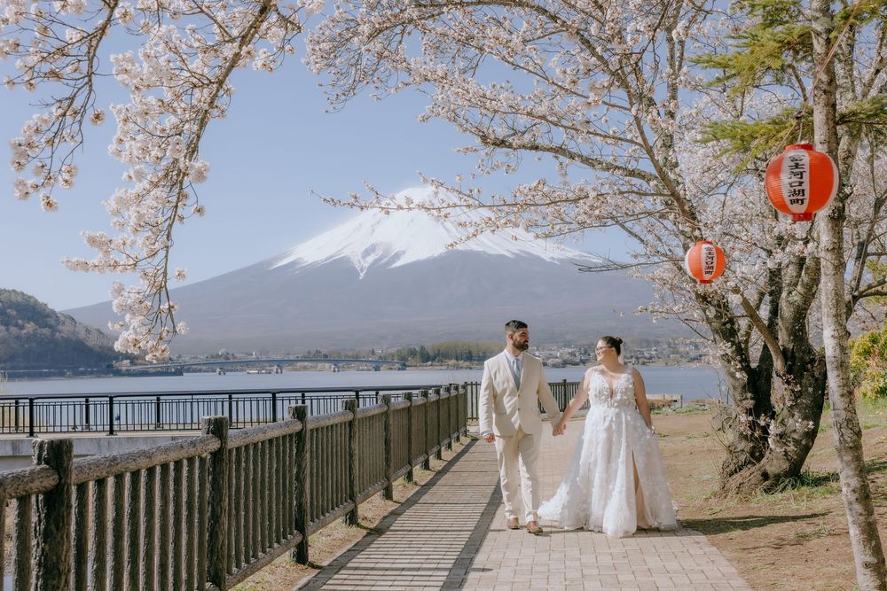 Scenic wedding photos taken at Mount Fuji with cherry blossoms and lake views along a railed pathway.