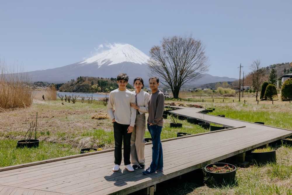 A group of people stand on a wooden boardwalk path overlooking snow-capped mountains in a scenic landscape.