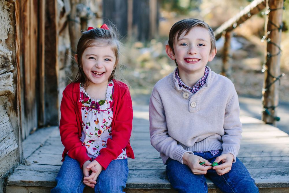 Two children sit together wearing red and gray sweaters in an outdoor setting.