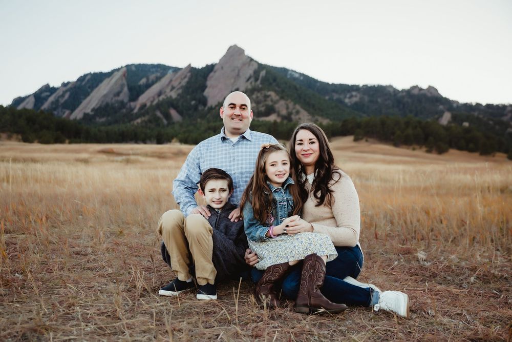 Family sitting together in field with mountain landscape backdrop.
