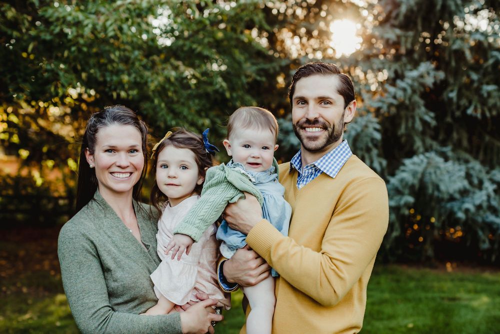 Family group poses together outdoors with green foliage in background at sunset.