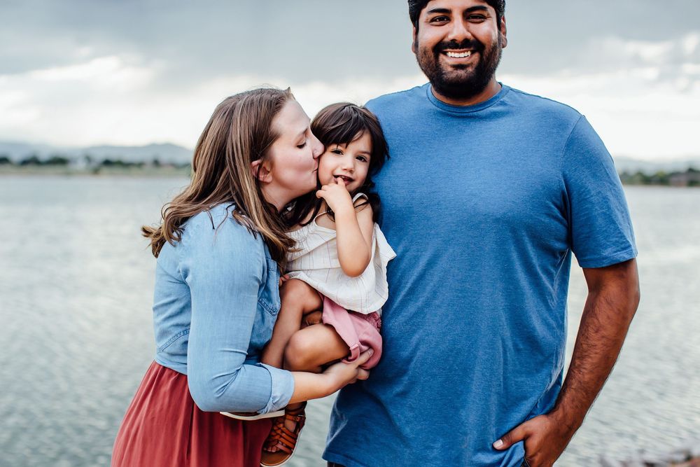 Family poses together along waterfront with cloudy sky backdrop.